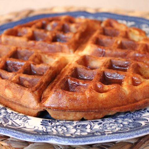 A buttermilk sourdough Belgian waffle drizzled with maple syrup on a blue stoneware plate.
