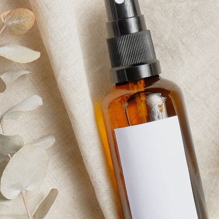 brown amber spray bottle with white label laying on natural linen fabric