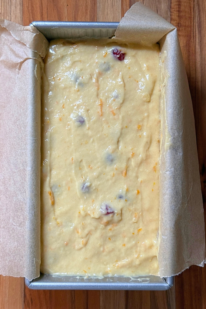 Cranberry orange bread batter spread into a parchment-lined loaf pan